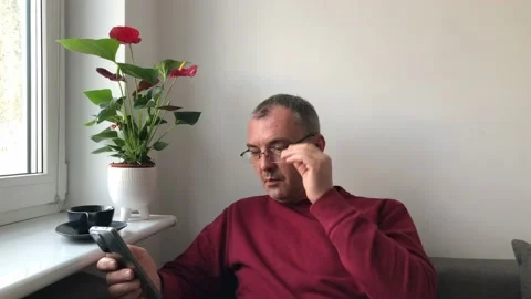 A gray-haired middle-aged man with glasses sits near a window talking on a video Stock Footage 231748320