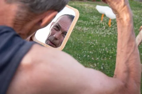 A gray-haired middle-aged man shaves his hair with a clipper in a garden Stock Photos