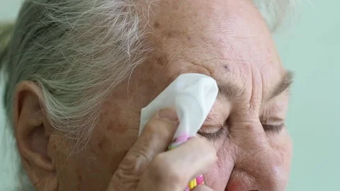 Gray-haired old lady wipes her sore eyes with a handkerchief Stock Footage 194523385