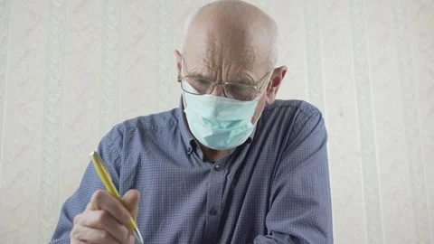 Gray haired old man with glasses sits at table and writes letter with pen Video stock 148438674