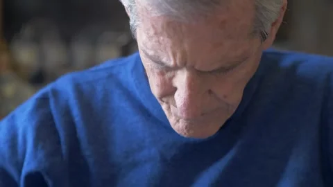 Gray haired pensioner reading book carefully at living room table indoors Stock Footage 334776293