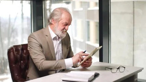 A gray- Haired Professor with a beard in a beautiful suit is sitting at a Desk Stock Photos