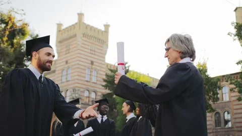 Gray-haired professor congratulating handsome male graduate and handing him a Stock Footage 83602680