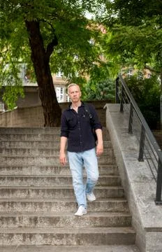 Gray-haired young man with a backpack goes down the stairs in the park. Stock Photos