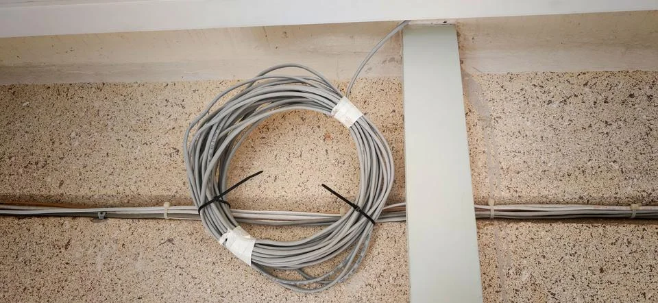 Gray internet cable coiled and secured with zip ties on a textured wall, high Stock Photos