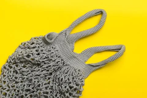 Gray knitted bag string bag lies on a yellow background. Stock Photos