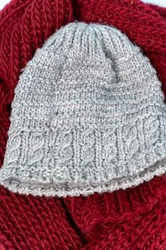 Gray knitted hat sits on a red scarf, showing a blend of colors and textures. Stock Photos