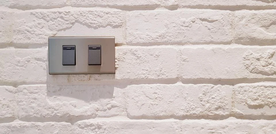 Gray light switch button installed on white rough or vintage wall 写真素材