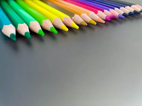 On a gray metal background, multi-colored pencils for drawing lie in one row. Stock Photos