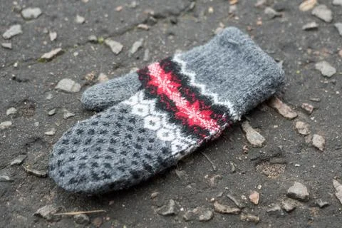 Gray mittens with pattern on a asphalt. Lost mitten. Stock Photos