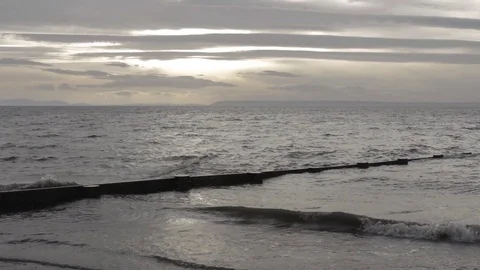 Gray ocean waves lapping against shore under a partially overcast afternoon sky. Stock Footage 98614727