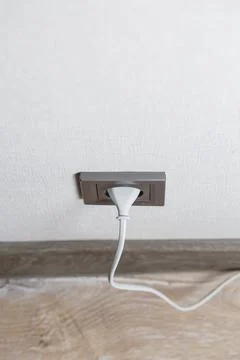 A gray outlet on the wall which includes a device with a white cord. Charging Stock Photos