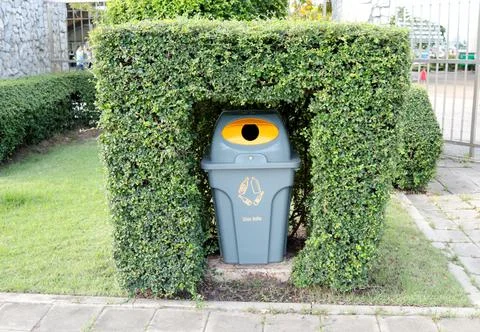 Gray plastic bin for glass bottle hide in shrub in garden. Foto stock