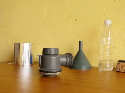 Gray plastic plumbing fitting placed on a table with containers and a funnel, Stock Photos