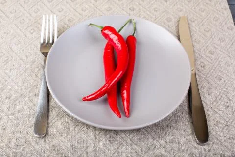 Gray plate with chilli red pepper on , spoon and knife on linen tablecloth Stock Photos