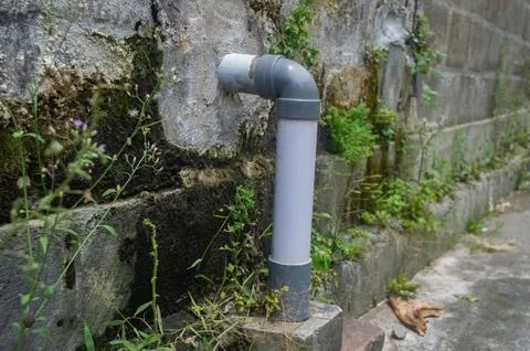 A gray PVC pipe and elbow fitting extends from a textured concrete wall ove.. Stock Photos