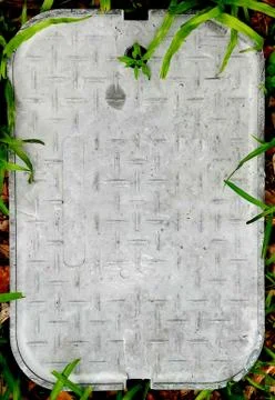 Gray Rectangular Sewer cover surrounded by grass Stock Photos