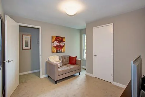 Gray room interior features a small tufted sofa accented with red pillows and Stock Photos
