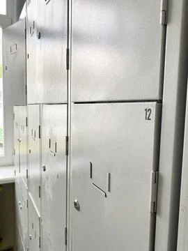 Gray school storage lockers lined against a wall with visible numbers, sunlight Stock Photos