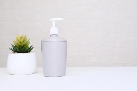 Gray soap dispenser and potted plant for spa, body and face care, bathroom Stock Photos