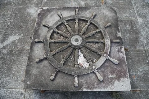 A gray stone square with an old ship's wheel in the center, lying on its si.. 스톡 사진