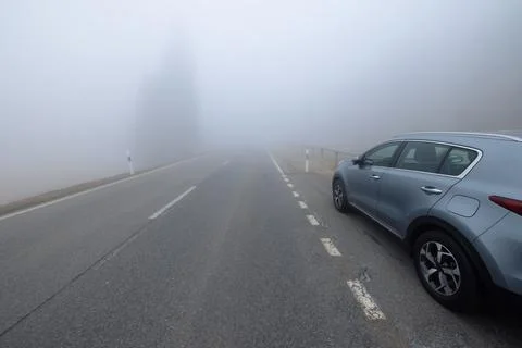 A gray SUV car is parked on the side of a straight empty road invaded by thick Stock Photos