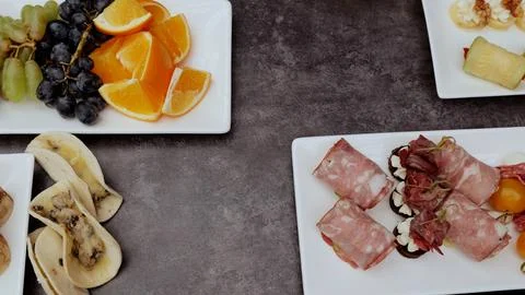 Gray table featuring appetizer spread, sliced oranges, grapes, meat rolls, mini Foto stock