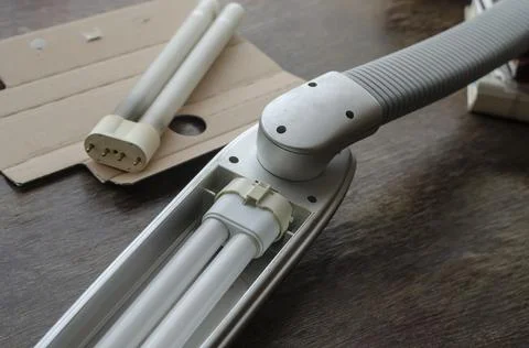 A gray table lamp with a new compact fluorescent bulb rests on a wooden table Stock Photos