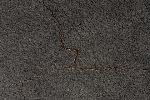 Gray wall with a crack. Texture of rough plaster with uneven granular coating Stock Photos