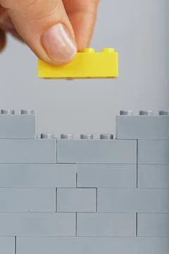 A gray wall made of a toy construction set with the last yellow brick in hand Stockfoto's