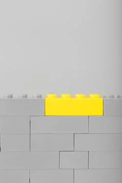 A gray wall made of a toy construction set with the last yellow brick Foto stock