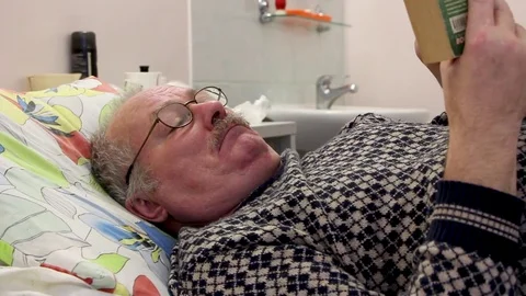 Graybeard gaffer old man on hosp bed read Stock Footage 81836579