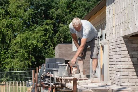 A grayhaired man saw bricks with a concrete saw of the right size for subsequent Stock Photos