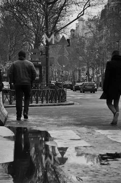 Grayscale shot of reflections in puddle, men walking by Paris Metro, France Foto stock