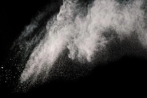 Grayscale of some brown particles exploding on black background, brown dust spla Stockfoto's