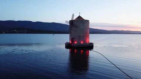 Grazing fast flight around A romantic windmill on a calm sea lagoon at sunset  Stock Footage 107847976