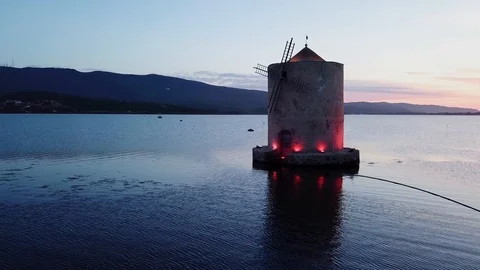 Grazing flight around A romantic windmill on a calm sea lagoon at sunset  Stock Footage 107847931