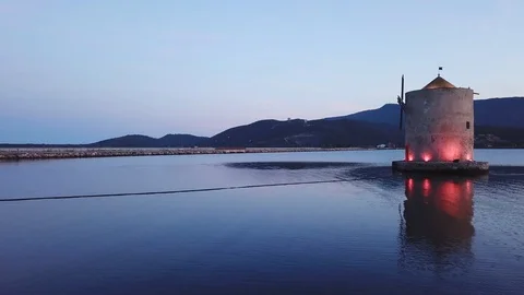 Grazing flight around A romantic windmill on a calm sea lagoon at dusk Stock Footage 107848246