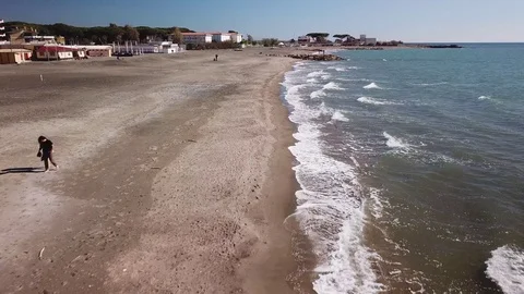 Grazing flight  over the sand beach of Tarquinia with buildings in the distance Stock Footage 106536271