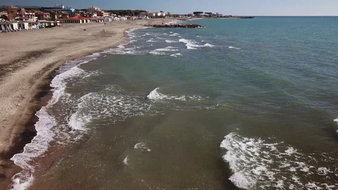 Grazing flight  over the sand beach of Tarquinia with buildings in the distance Stock Footage 106537017