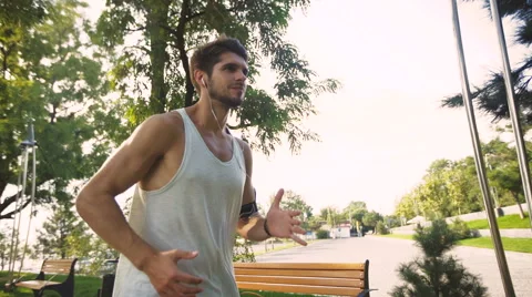 Great active young man jogging on park, while listening to music in earphones Video stock 68857922