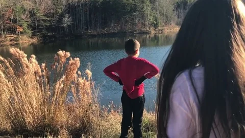 Great slow motion of kids approaching another kid in front of a lake and hugging Stock Footage 83097611