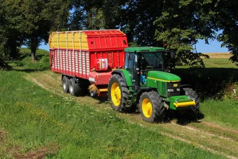 Greed tractor with self loading wagon filled with straw on dirt road betwee.. Stock Photos