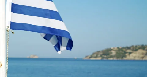 Greek flag flying on the wind flutters with sea and island in background, Greece Video stock 141010153