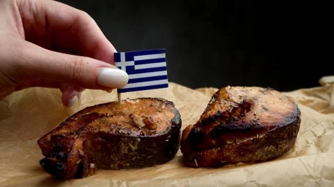 Greek flag stuck into fish steak, symbol of Mediterranean seafood from Greek Stock Footage 323010211