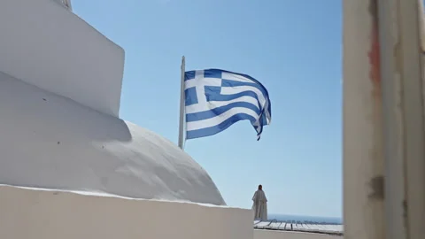 Greek Flag Waving Beside Whitewashed Rooftop and Lone Figure Stockbeeldmateriaal 341472396