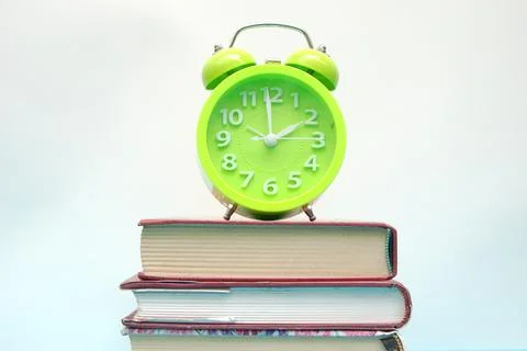 Green alarm clock and stack of books on blue table Stock Photos