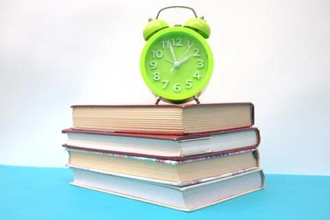 Green alarm clock and stack of books on blue table Stock Photos