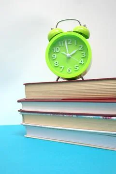 Green alarm clock and stack of books on blue table Stock Photos