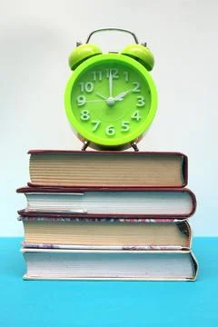 Green alarm clock and stack of books on blue table Stock Photos